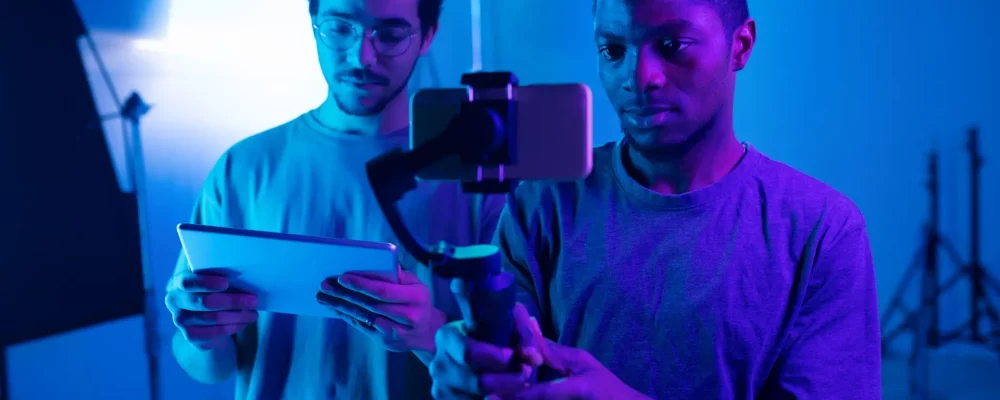 African American young operator making content with smartphone with director controlling the process using digital tablet